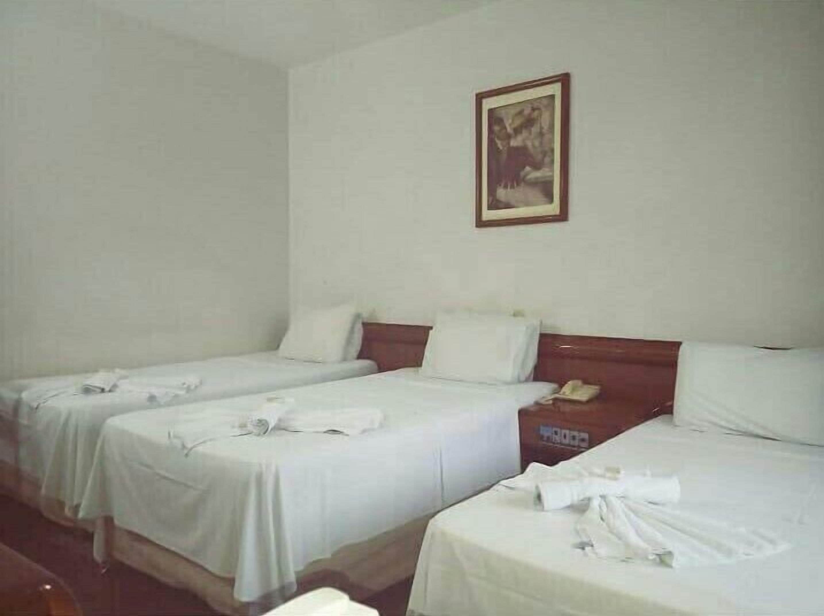 Une chambre d’hôtel avec deux lits simples, une tête de lit en bois, un tableau encadré au mur et un téléphone sur la table de chevet.