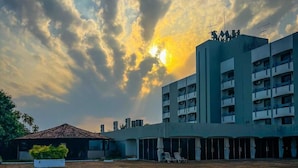 A swimming pool with a brick border, a building with multiple balconies, and a sunset in the background. - Santa Maria Hotel (Acailandia)