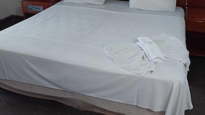 A neatly made bed with white linens, a wooden headboard, and a bedside table with a lamp. - Santa Maria Hotel (Acailandia)