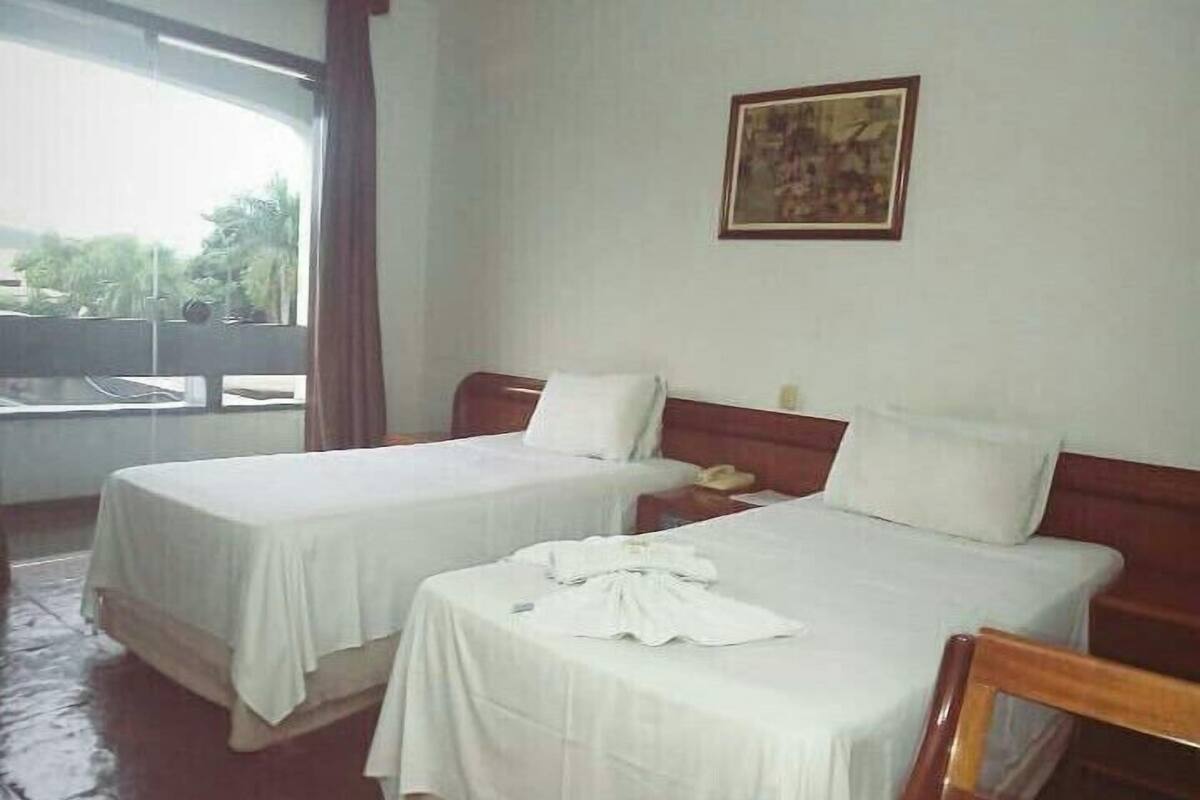 A hotel room with two beds, a wooden headboard, a painting on the wall, and a view through a window.