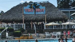 Ein Poolbereich mit einem Schild, das „TIKI HUT POOL BAR“ zeigt, und einer mit Reet gedeckten Struktur im Hintergrund.