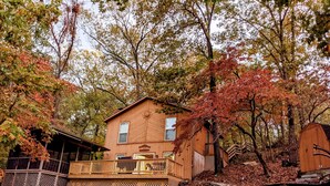 Eine Holzhütte mit einer Terrasse, umgeben von Bäumen im Herbstlaub.