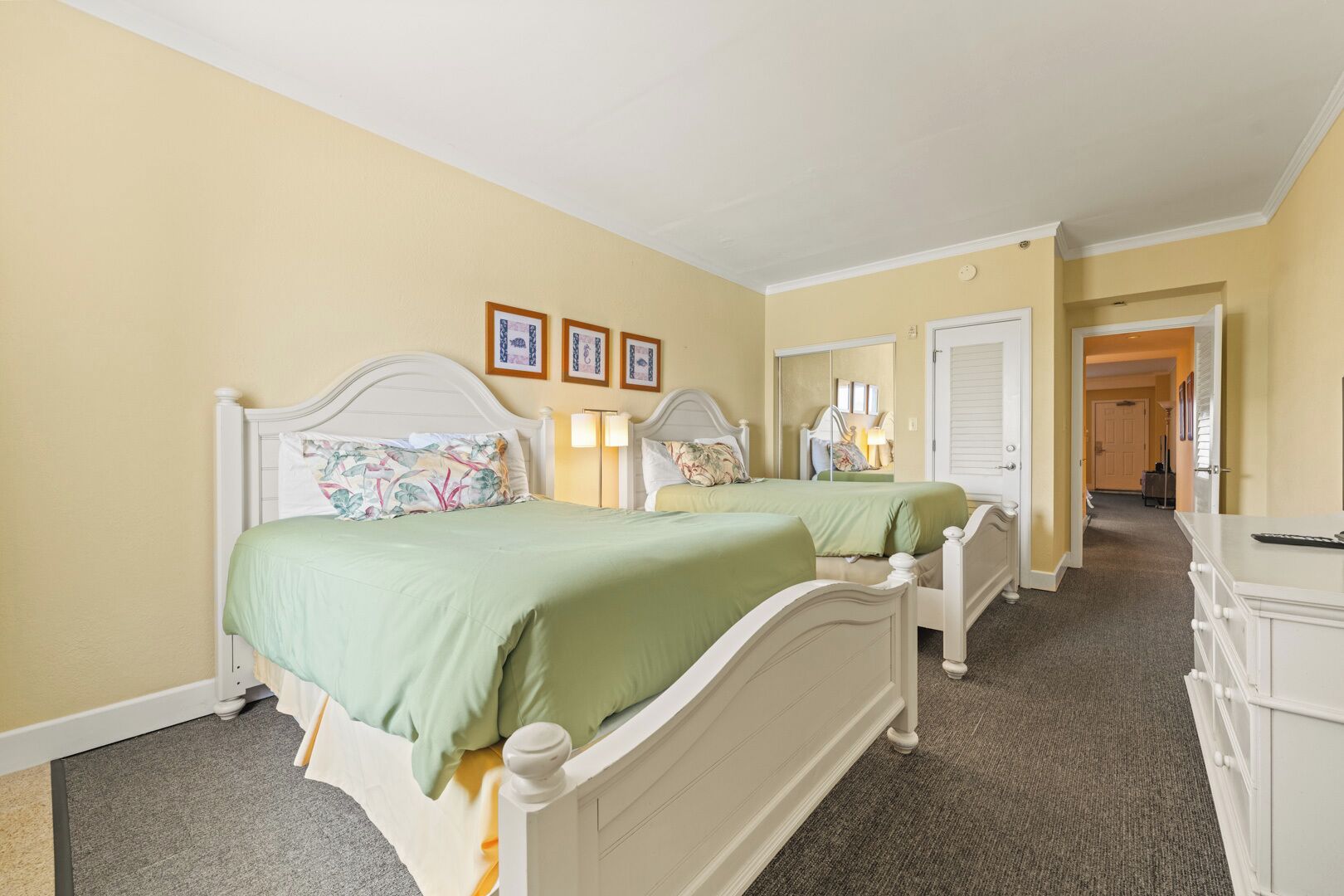 A bedroom with two beds, a dresser, and a hallway leading to another room.