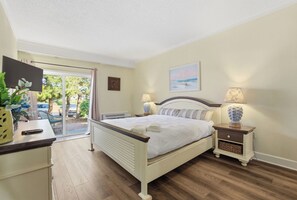 A bedroom with a bed, bedside lamps, a TV, and a view of the outdoors. - The Villas at Hatteras Landing by Kees Vacations (Hatteras)