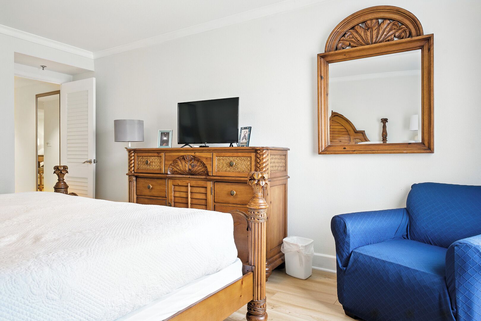 Une chambre à coucher avec un lit, une commode, un téléviseur, un miroir et une chaise bleue.