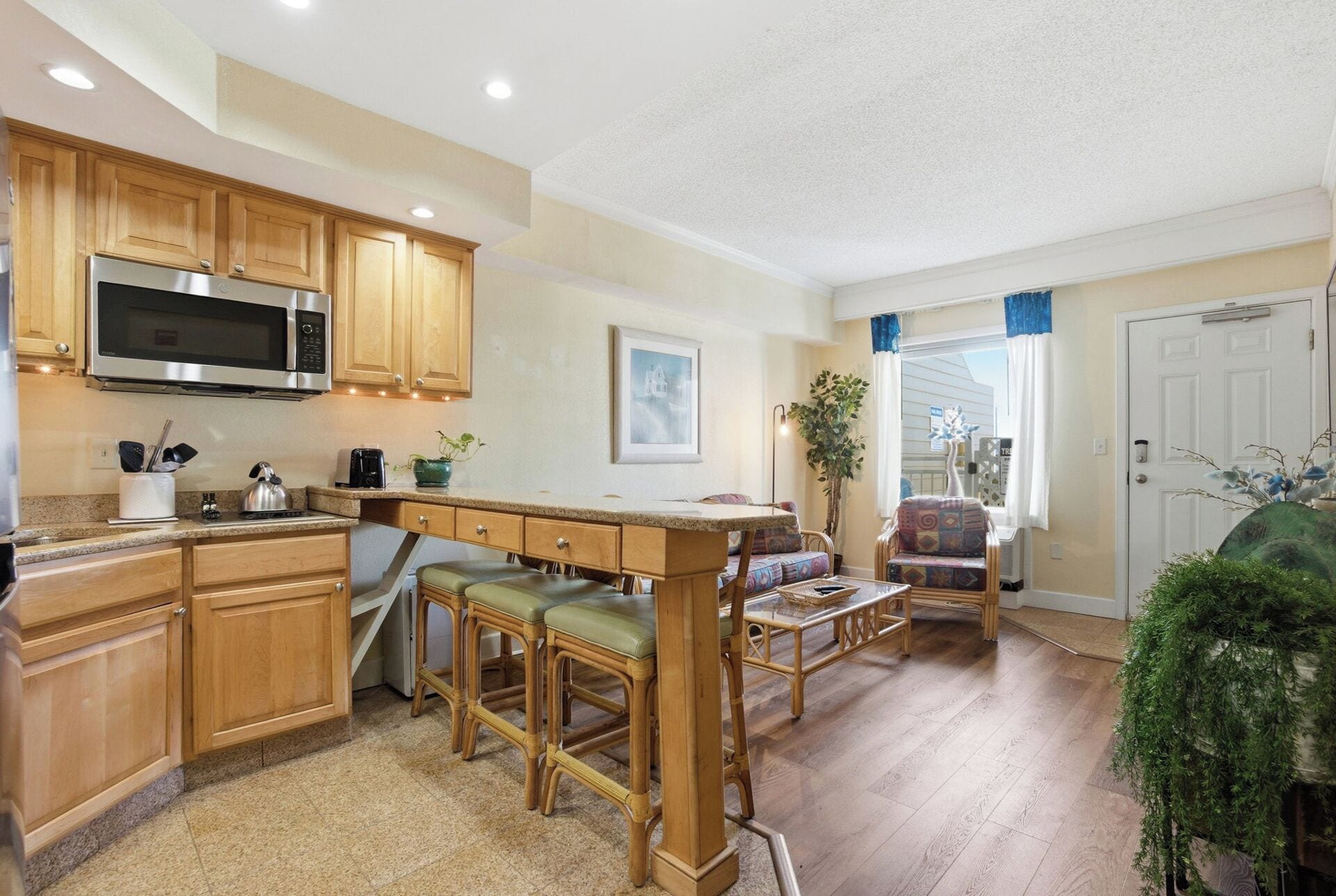 A kitchen with wooden cabinets, a microwave, and a bar stool area.