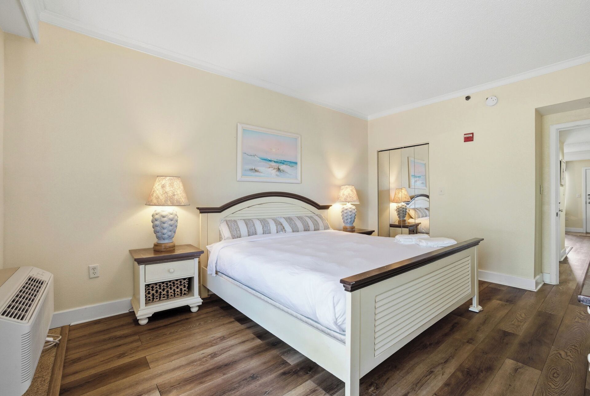 A bedroom with a bed, bedside lamps, a heater, and a painting on the wall.
