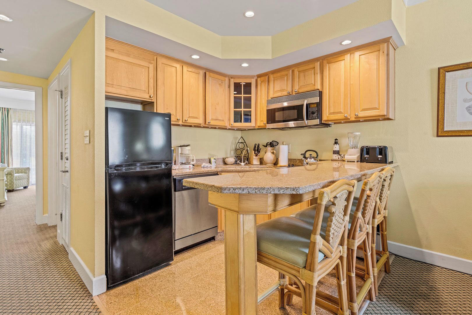 A kitchen with wooden cabinets, a black refrigerator, stainless steel appliances, and a bar area with chairs.