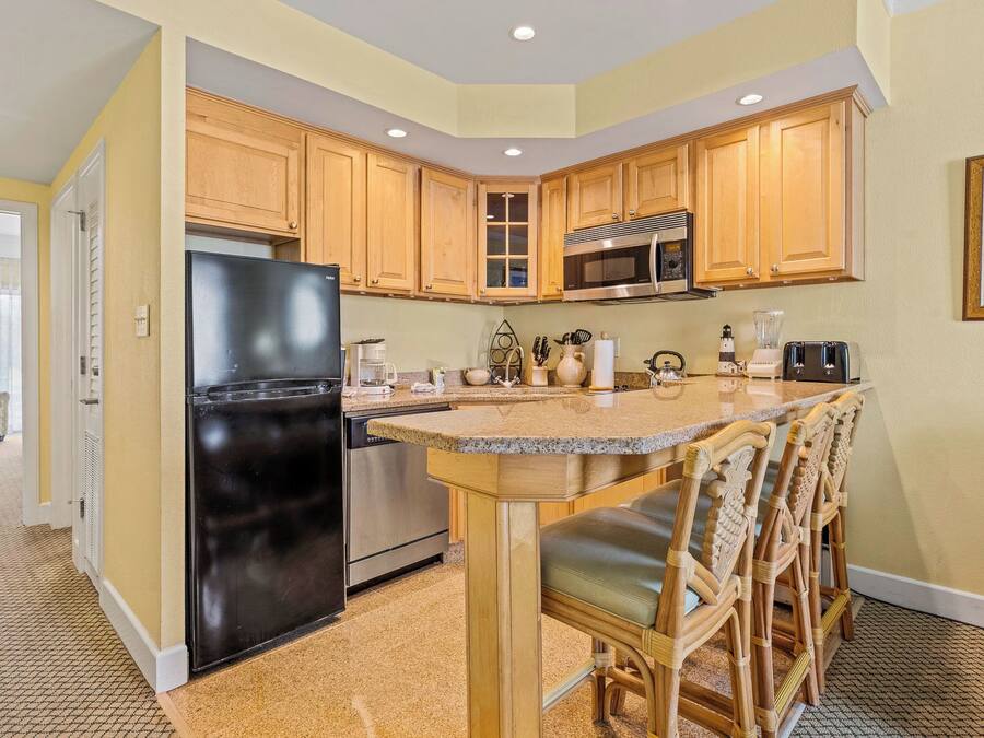A kitchen with wooden cabinets, a black refrigerator, stainless steel appliances, and a bar area with chairs.