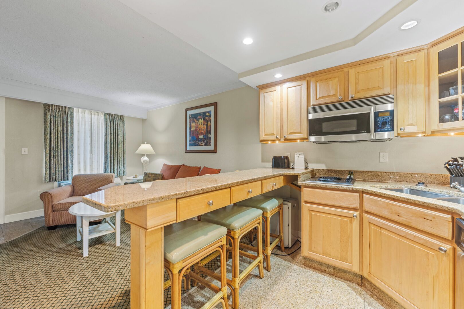 A compact kitchen with wooden cabinets, a built-in microwave, and a bar stool area.