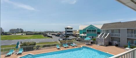 A pool area with lounge chairs and a view of a parking lot and buildings in the background.