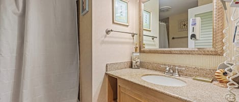 A bathroom with a shower curtain, two sinks, a mirror, and a towel rack.