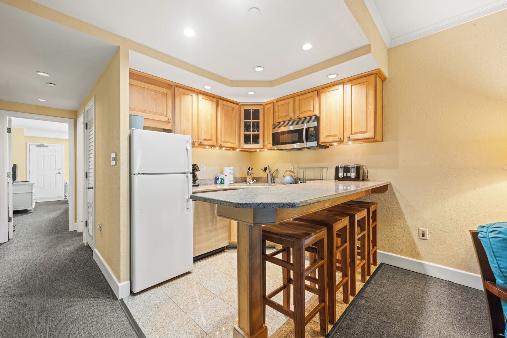 Una cocina moderna con armarios de madera, microondas integrado, refrigerador y una zona de bar con taburetes.