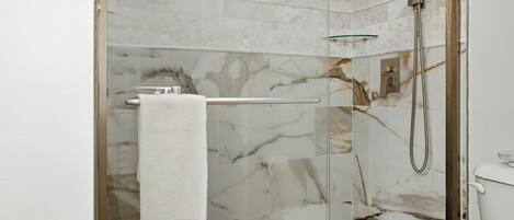 Un baño moderno con ducha de vidrio, baldosas de mármol y un perchero para toallas.
