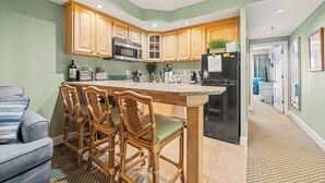 A kitchen with wooden cabinets, a central island with bar stools, a refrigerator, and a microwave. - The Villas at Hatteras Landing by Kees Vacations (Hatteras)