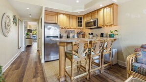 A kitchen with wooden cabinets, a stainless steel refrigerator, a microwave, and a bar area with wicker chairs. - The Villas at Hatteras Landing by Kees Vacations (Hatteras)