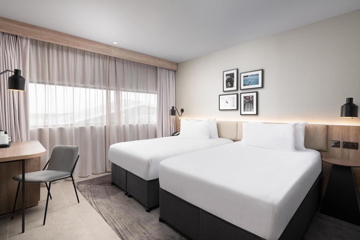 Ein Hotelzimmer mit zwei Betten, einem Schreibtisch, einem Stuhl und einem fenster mit Vorhängen.