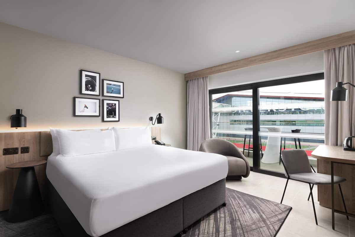 Ein modernes Hotelzimmer mit einem großen Bett, einem Schreibtisch, einem Stuhl und einem Balkon mit Blick auf ein Gebäude.