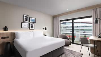 Una habitación de hotel moderna con una cama grande, un escritorio, una silla y un balcón con vistas a un edificio.