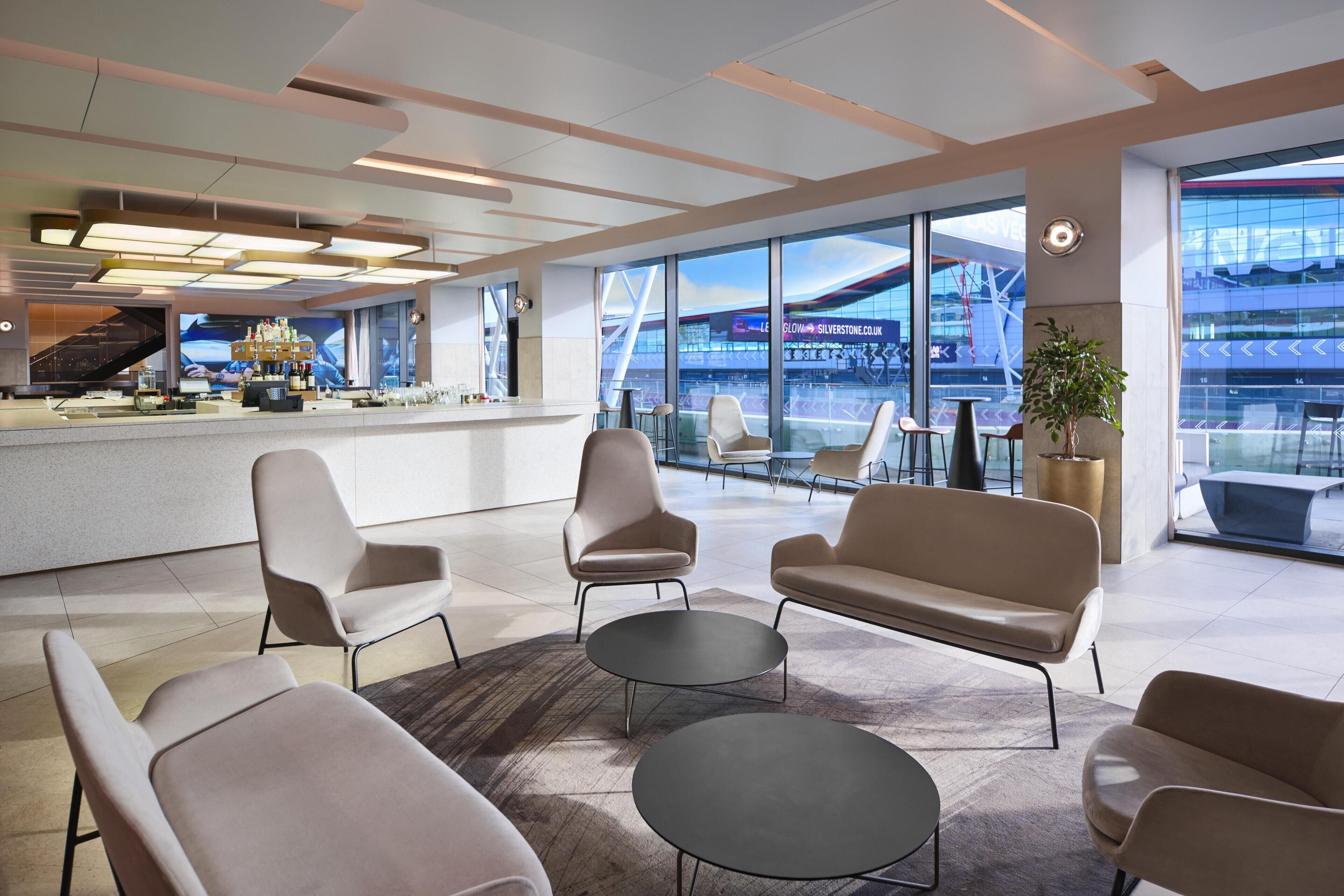 A modern hotel lobby with a bar area, seating, and large windows offering a view of a stadium.