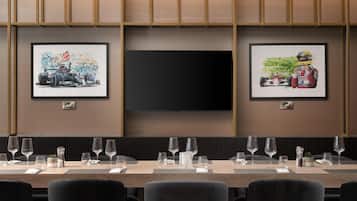 A conference room with a long table set for a meeting, framed artwork on the walls, and a flat-screen TV.