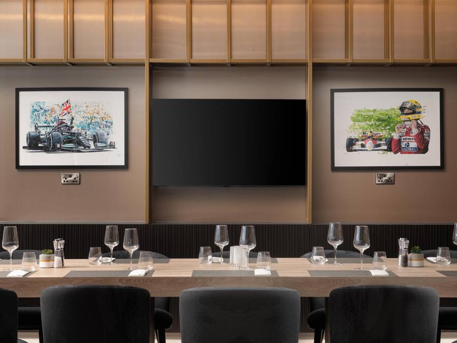 A conference room with a long table set for a meeting, framed artwork on the walls, and a flat-screen TV.