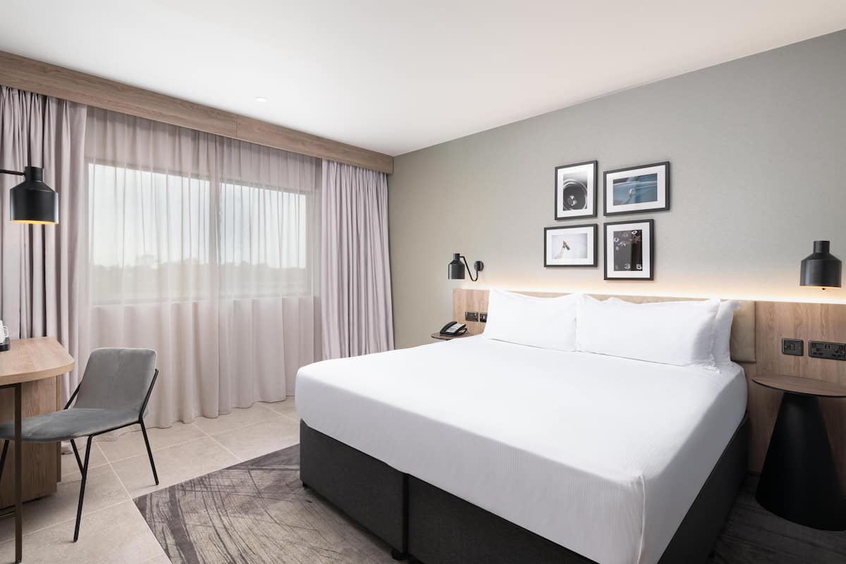 Ein Hotelzimmer mit einem großen Bett, einem Schreibtisch, einem Stuhl, einer Lampe und einem Nachttisch.
