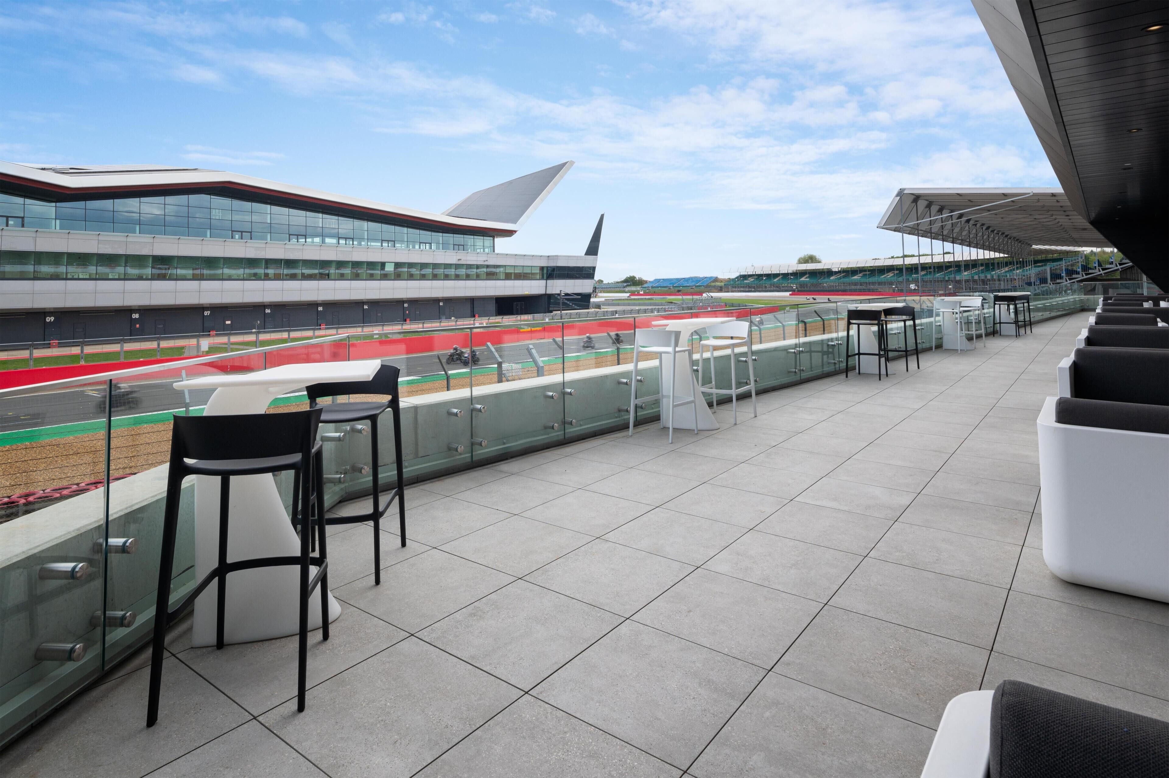 A modern building with a unique roof design, a race track, and outdoor seating with tables and chairs.