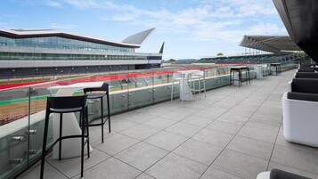 A modern building with a unique roof design, a race track, and outdoor seating with tables and chairs.