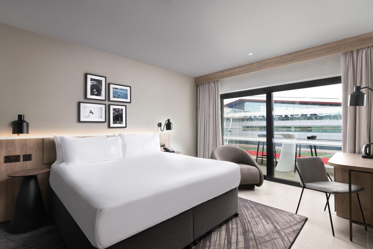 Une chambre d’hôtel avec un grand lit, un bureau, une chaise, une lampe et une vue sur un immeuble par la fenêtre.