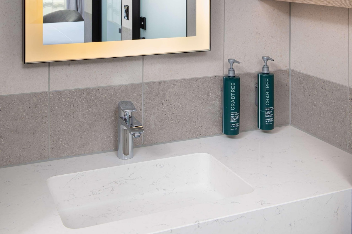 A bathroom with a large mirror, a sink, two hand soap dispensers, and a towel rack.