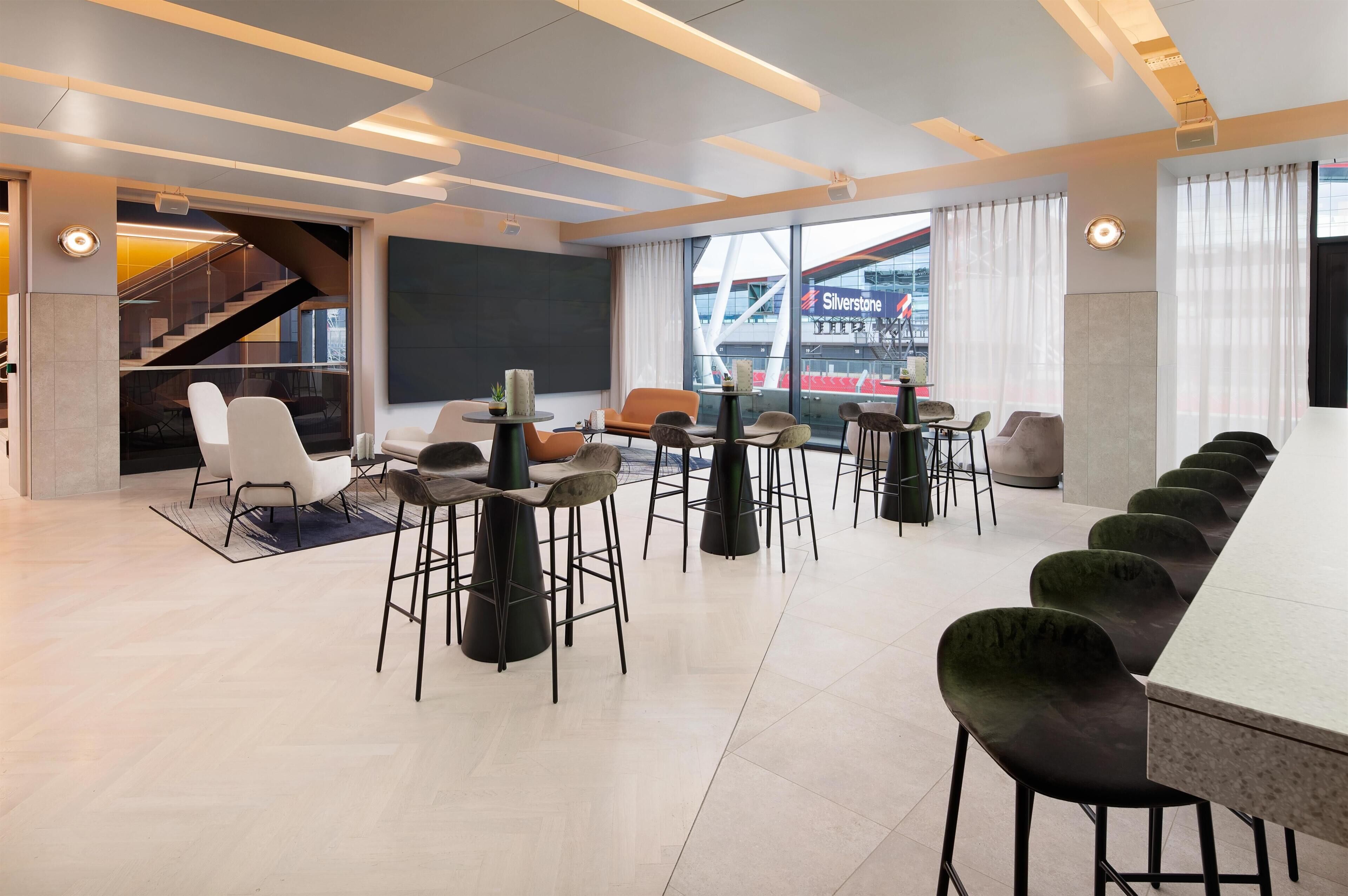 A modern hotel lobby with a long dining table, multiple chairs, a staircase, and large windows with a view of a bridge.
