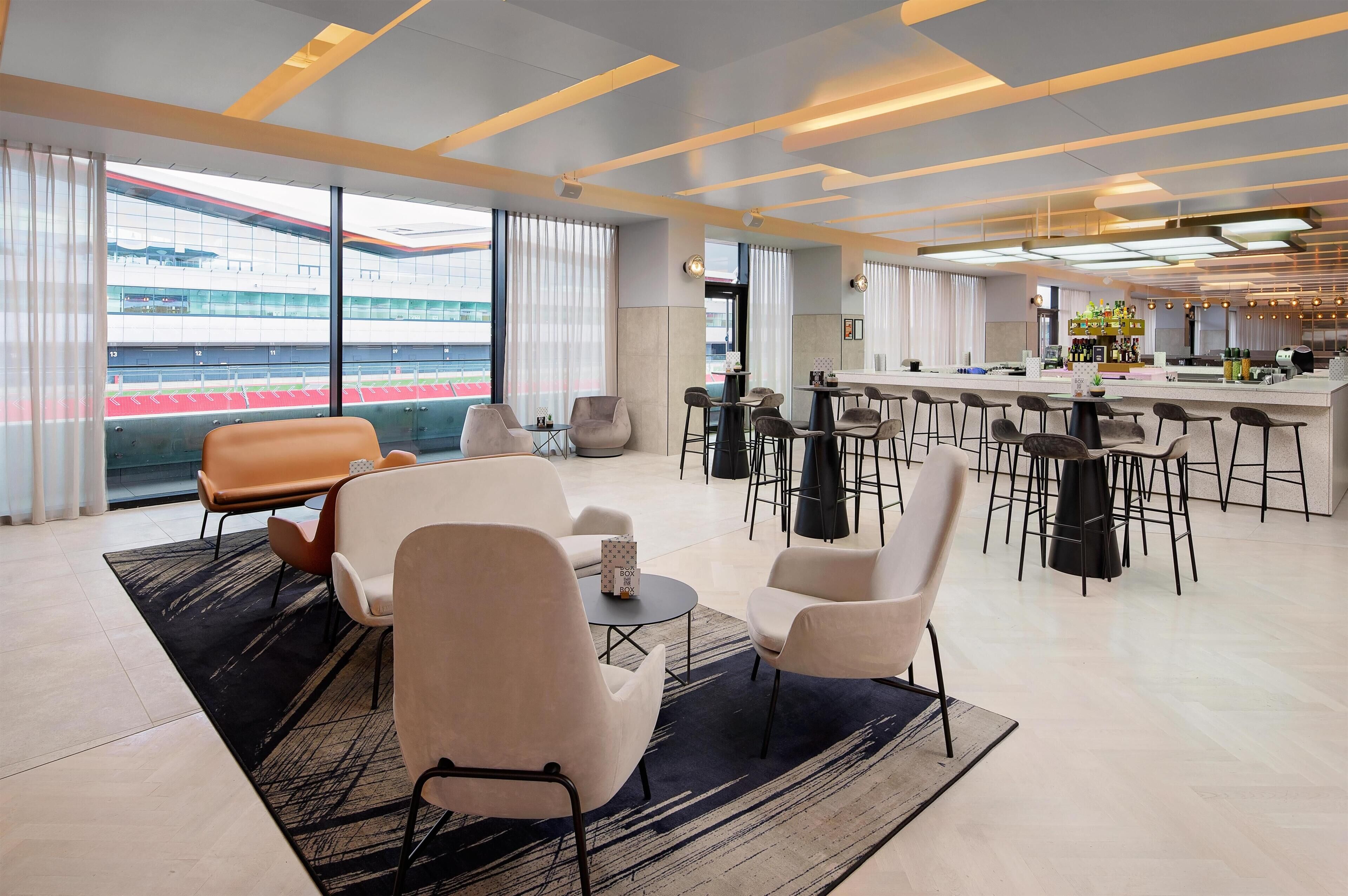 A modern hotel lobby with seating areas, a bar, and large windows offering views of a stadium.