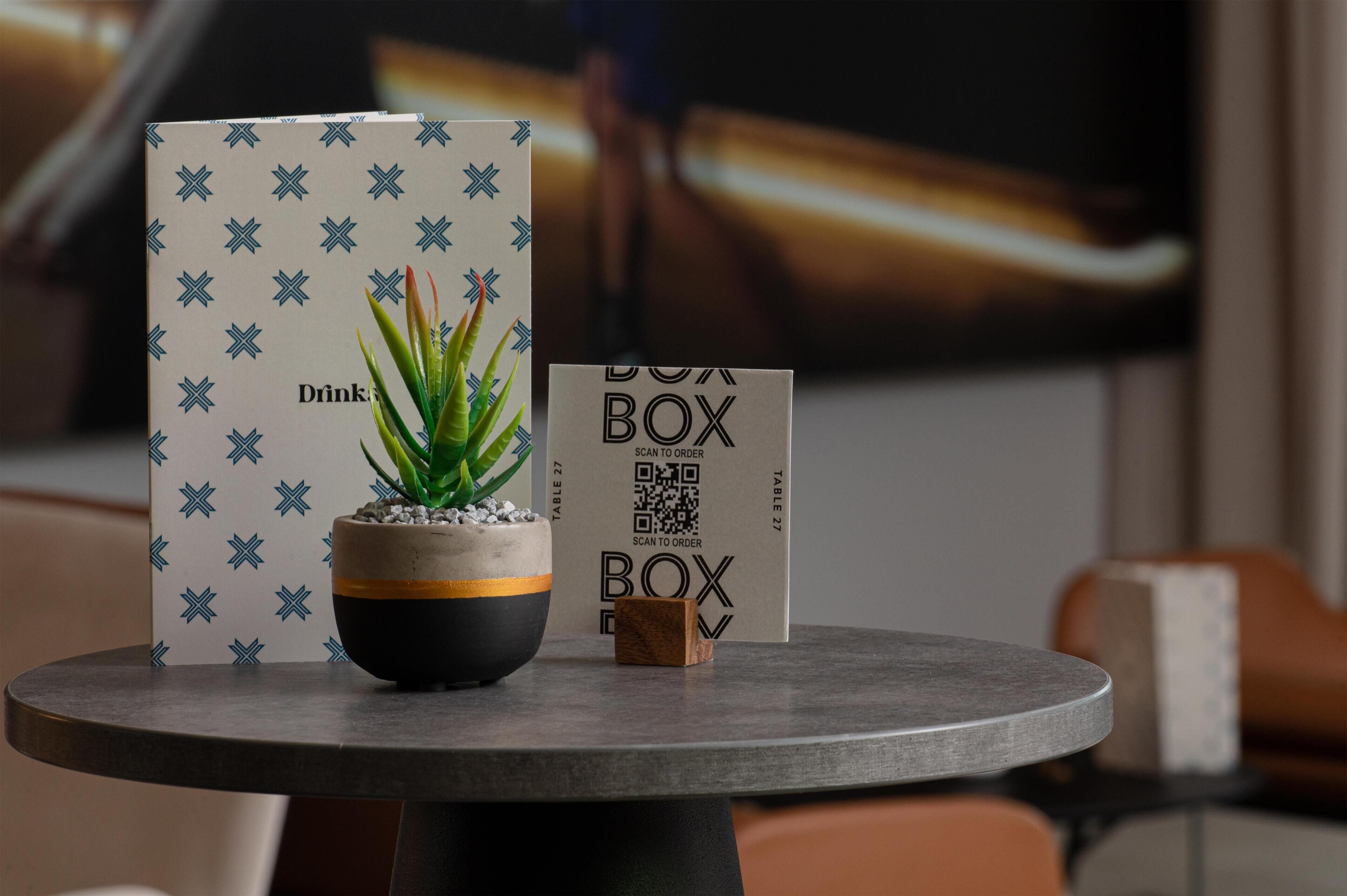 A table with a potted plant, a drink card, and a box with a QR code.
