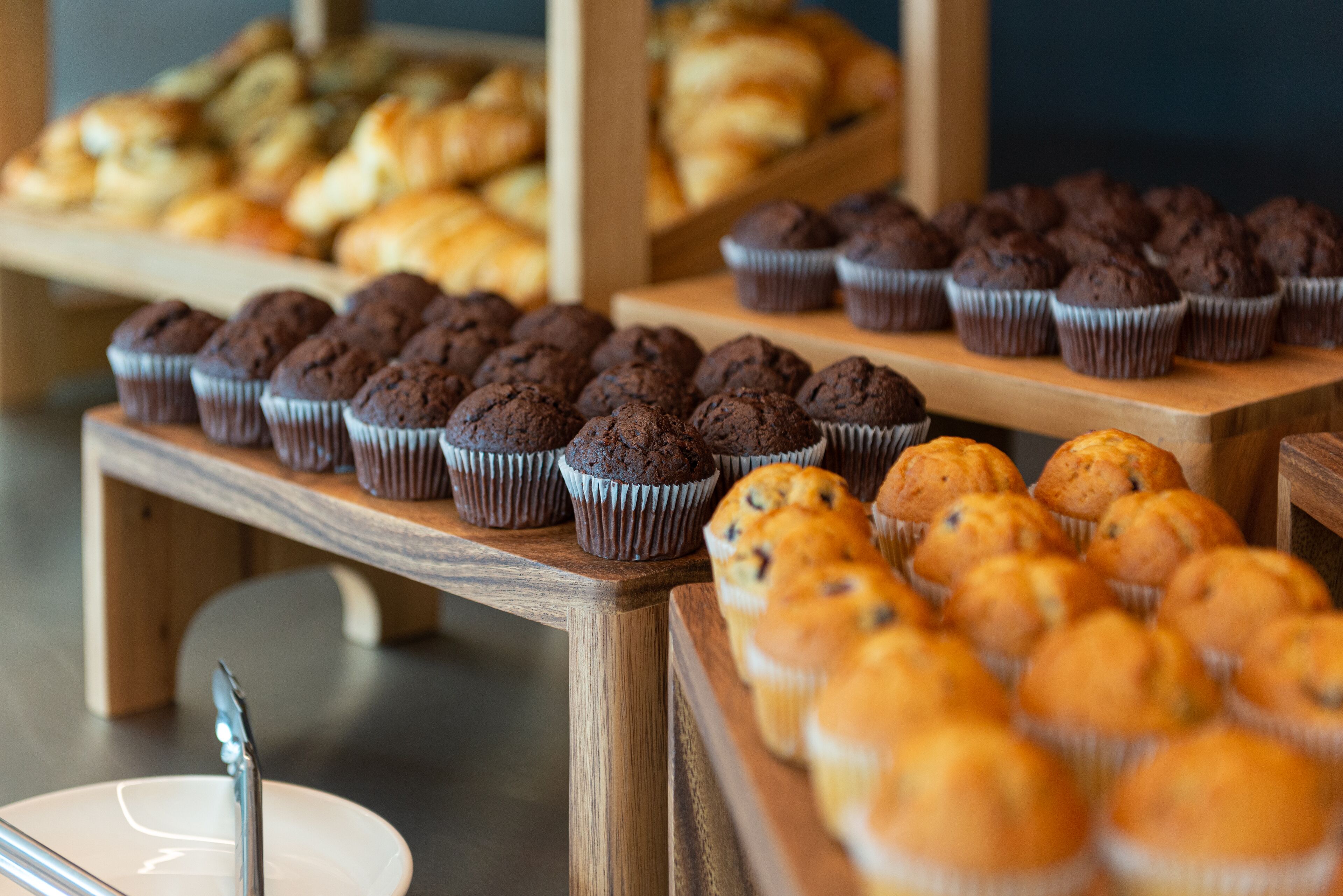 A bakery display with various baked goods, including muffins and pastries, arranged on wooden shelves.