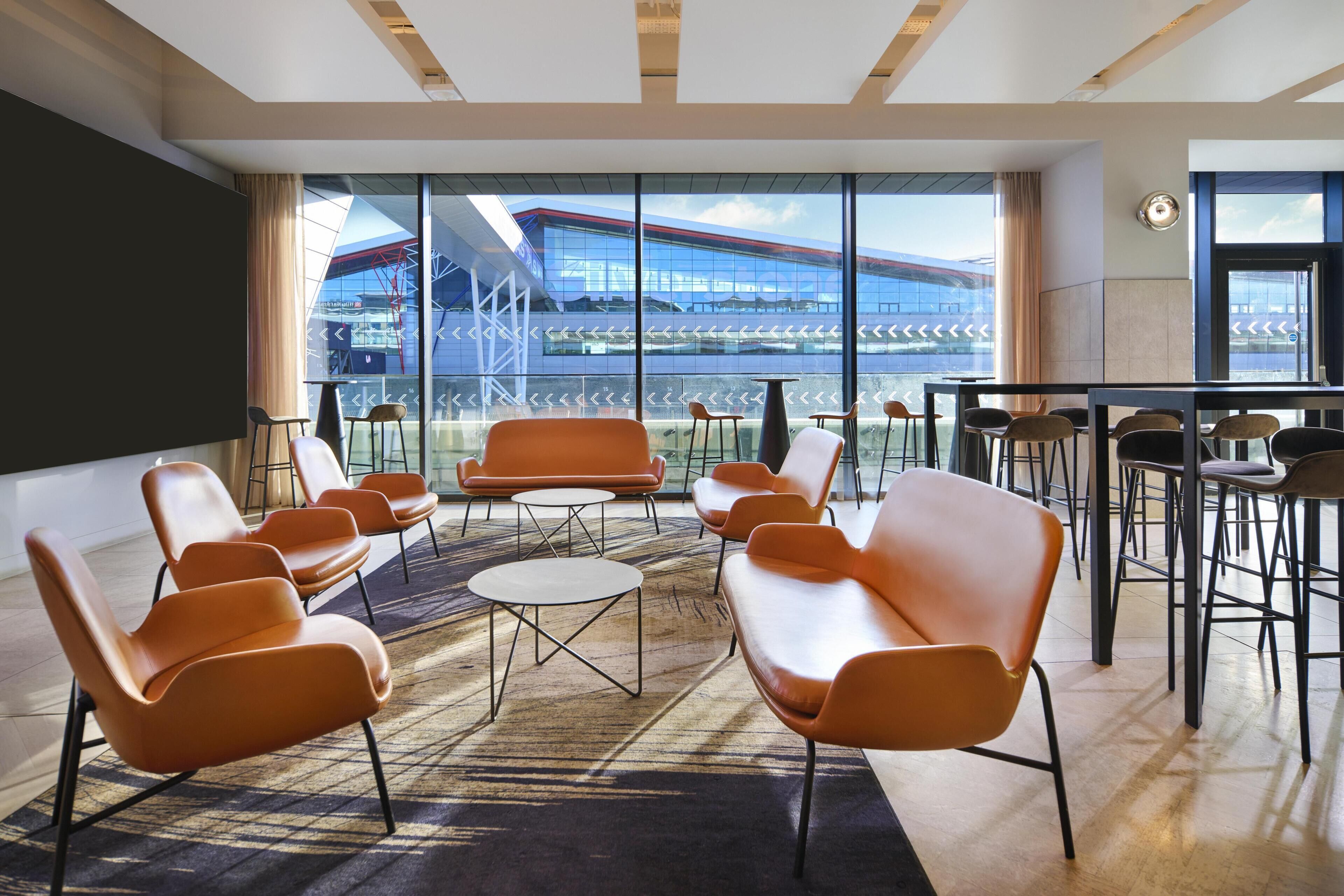 Una sala de conferencias moderna con sillas anaranjadas, una mesa redonda y ventanas amplias con vistas a un edificio.