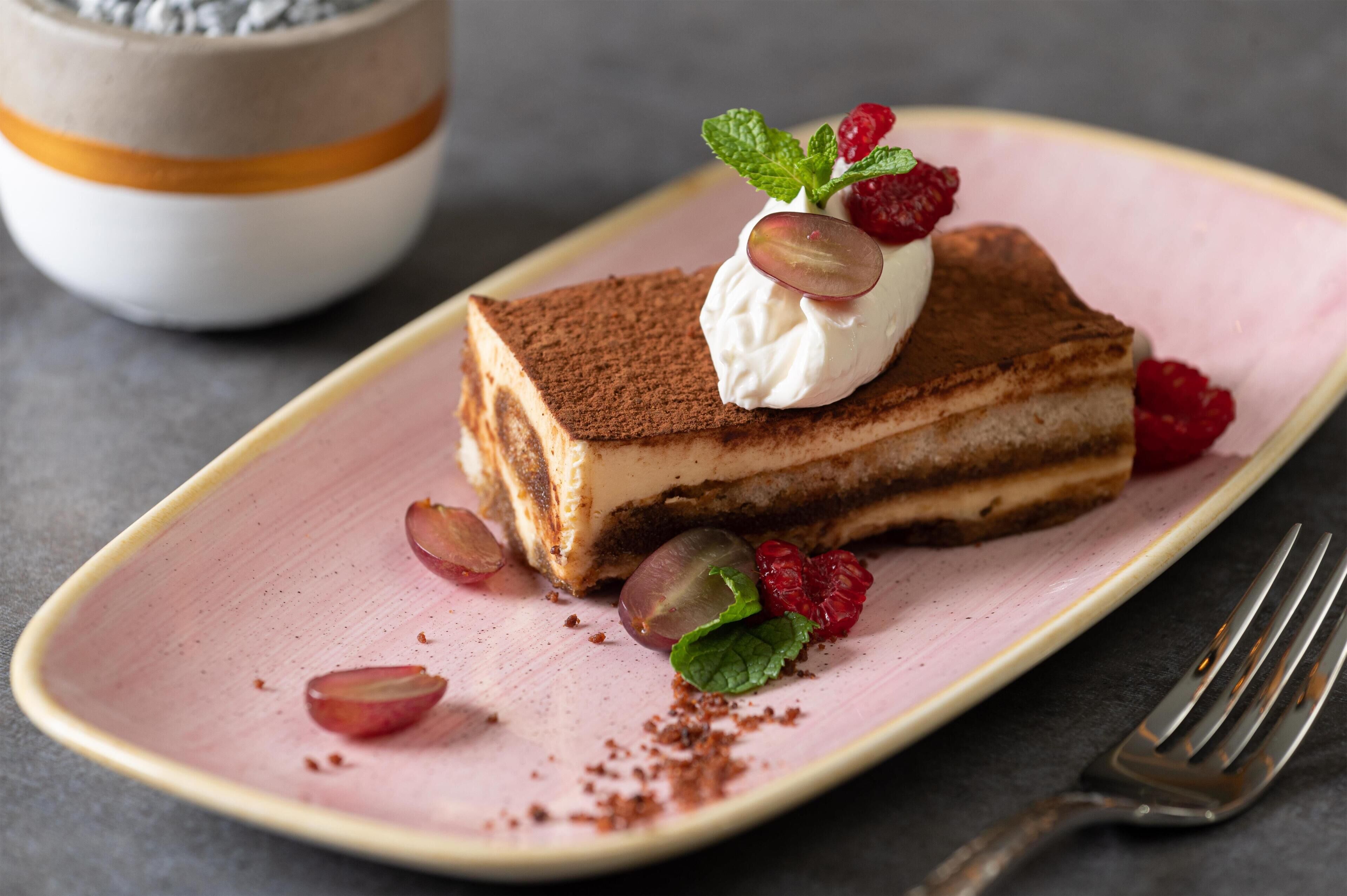 A slice of layered dessert on a pink plate with mint leaves and raspberries.