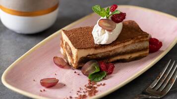 A slice of layered dessert on a pink plate with mint leaves and raspberries.