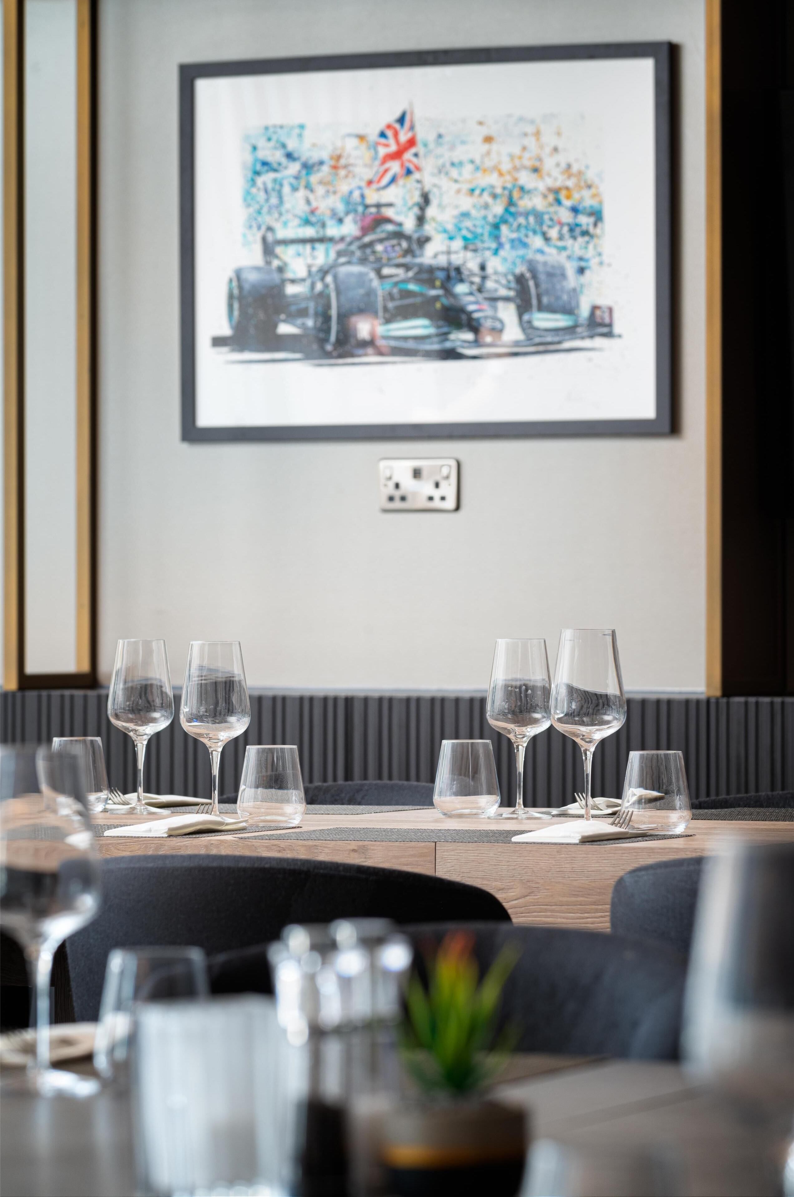 A dining area with a table set for four, glasses, and a framed artwork on the wall.