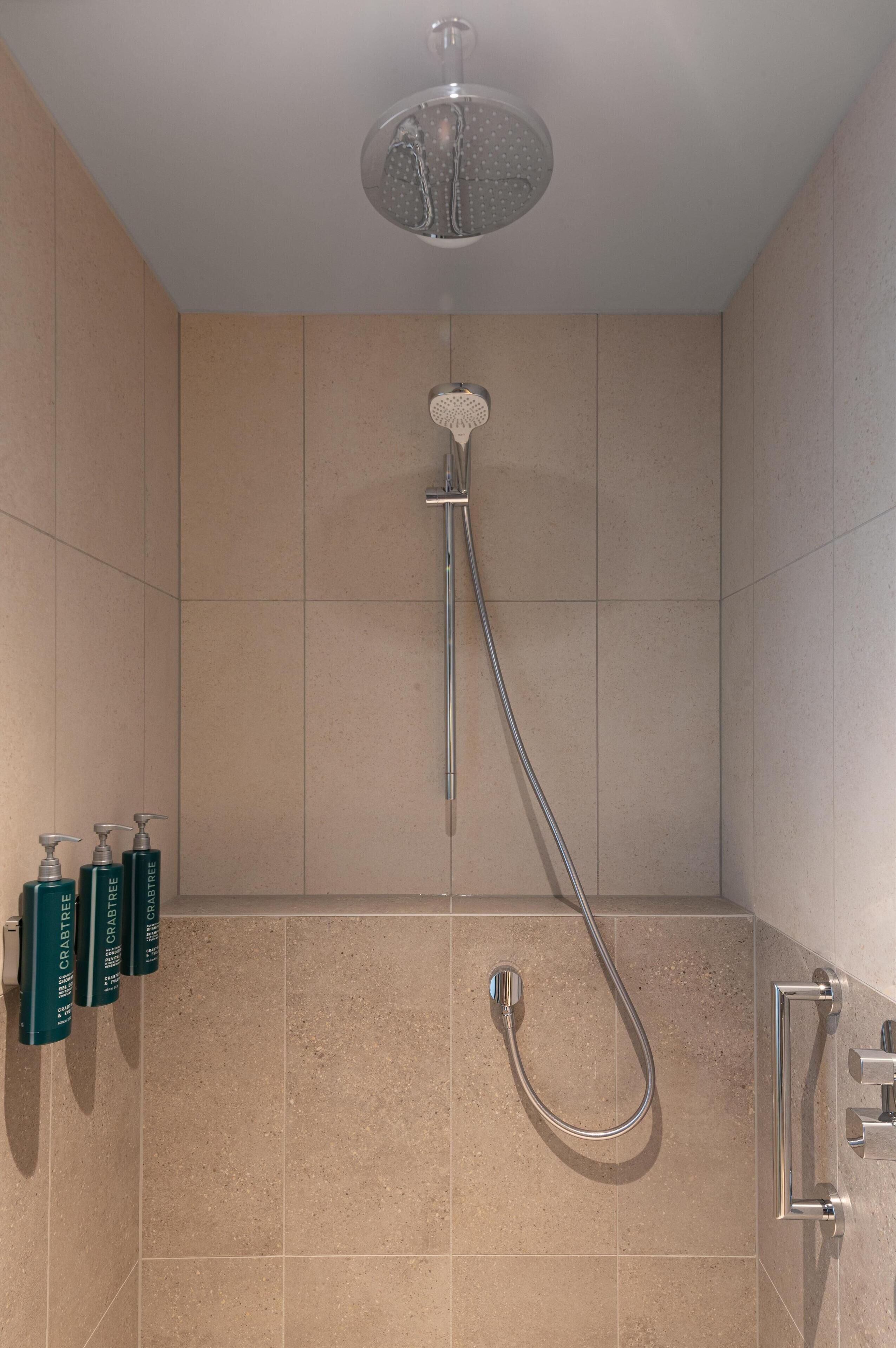 A shower with a handheld showerhead, a wall-mounted faucet, and a handheld showerhead.