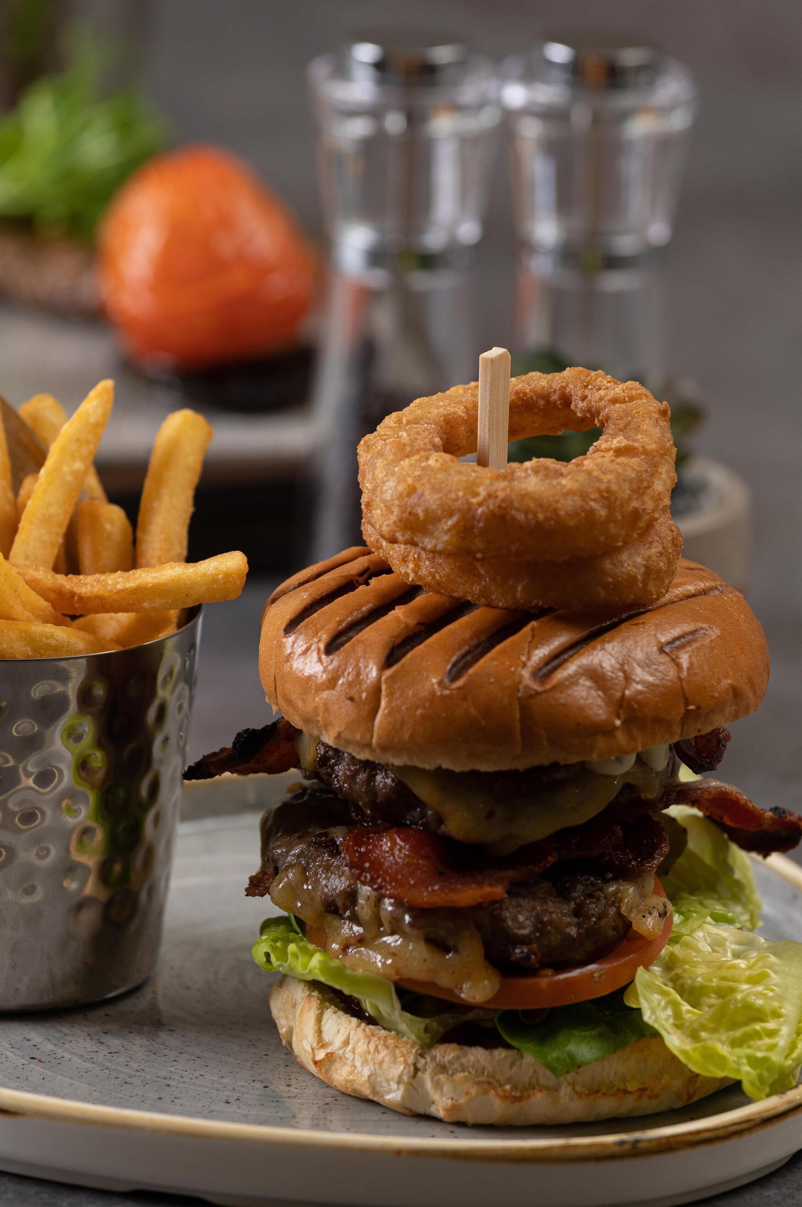 Een hamburger met broodje, sla, tomaat, kaas en spek, vergezeld van frietjes en een klein bekertje.