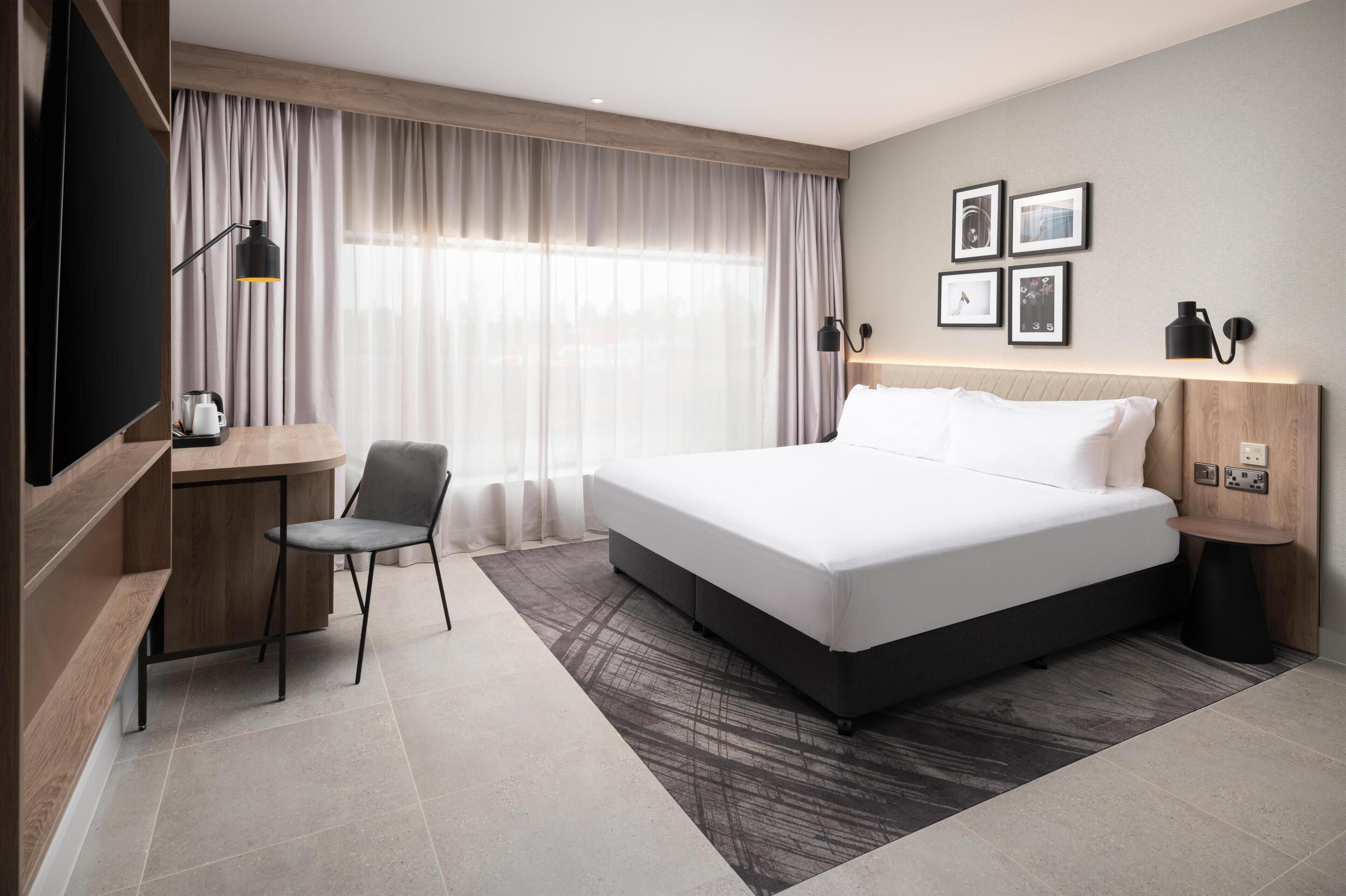 Habitación de hotel con cama, escritorio, silla, televisor y cortinas.