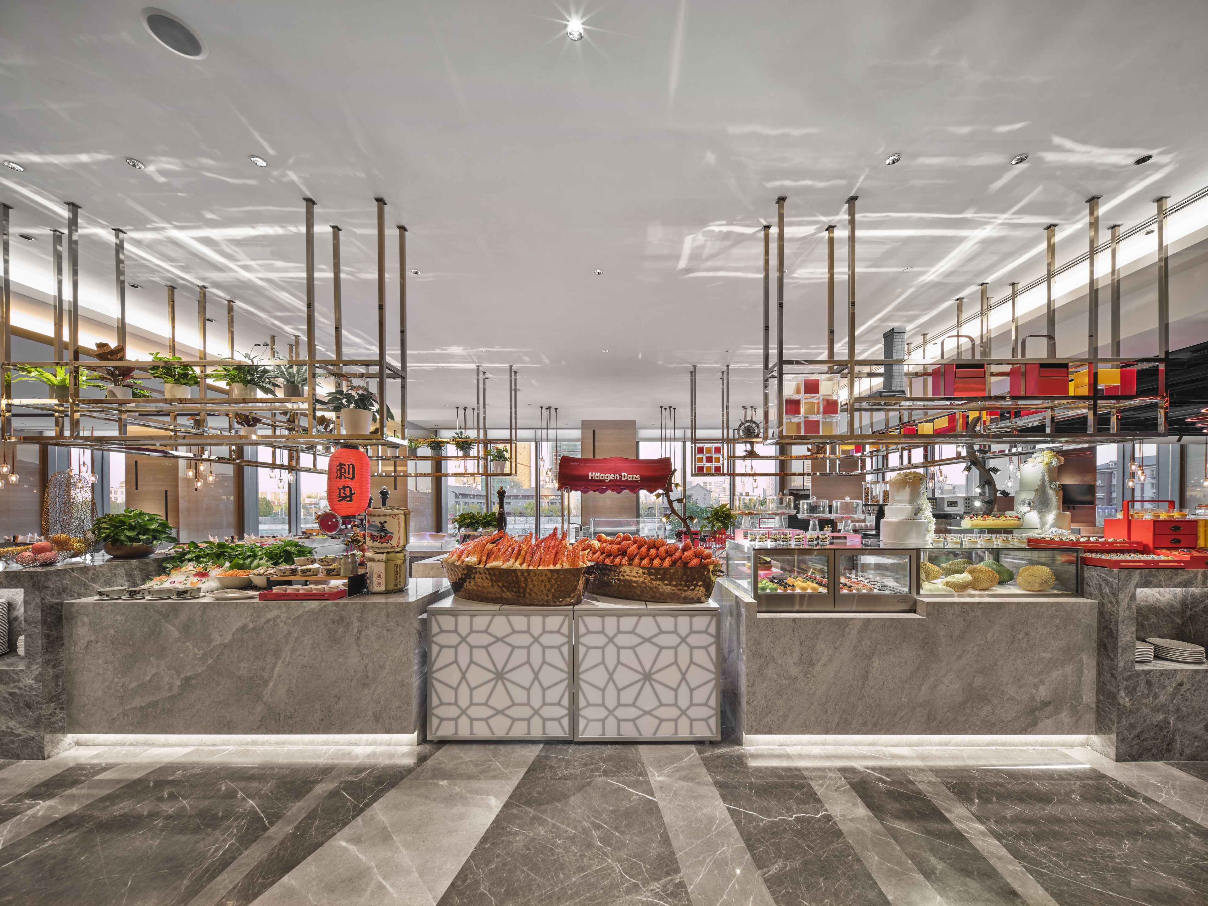 Un hall d’hôtel moderne avec un sol en marbre, un comptoir d’accueil central et divers équipements, notamment un présentoir de nourriture et des plantes en pot.