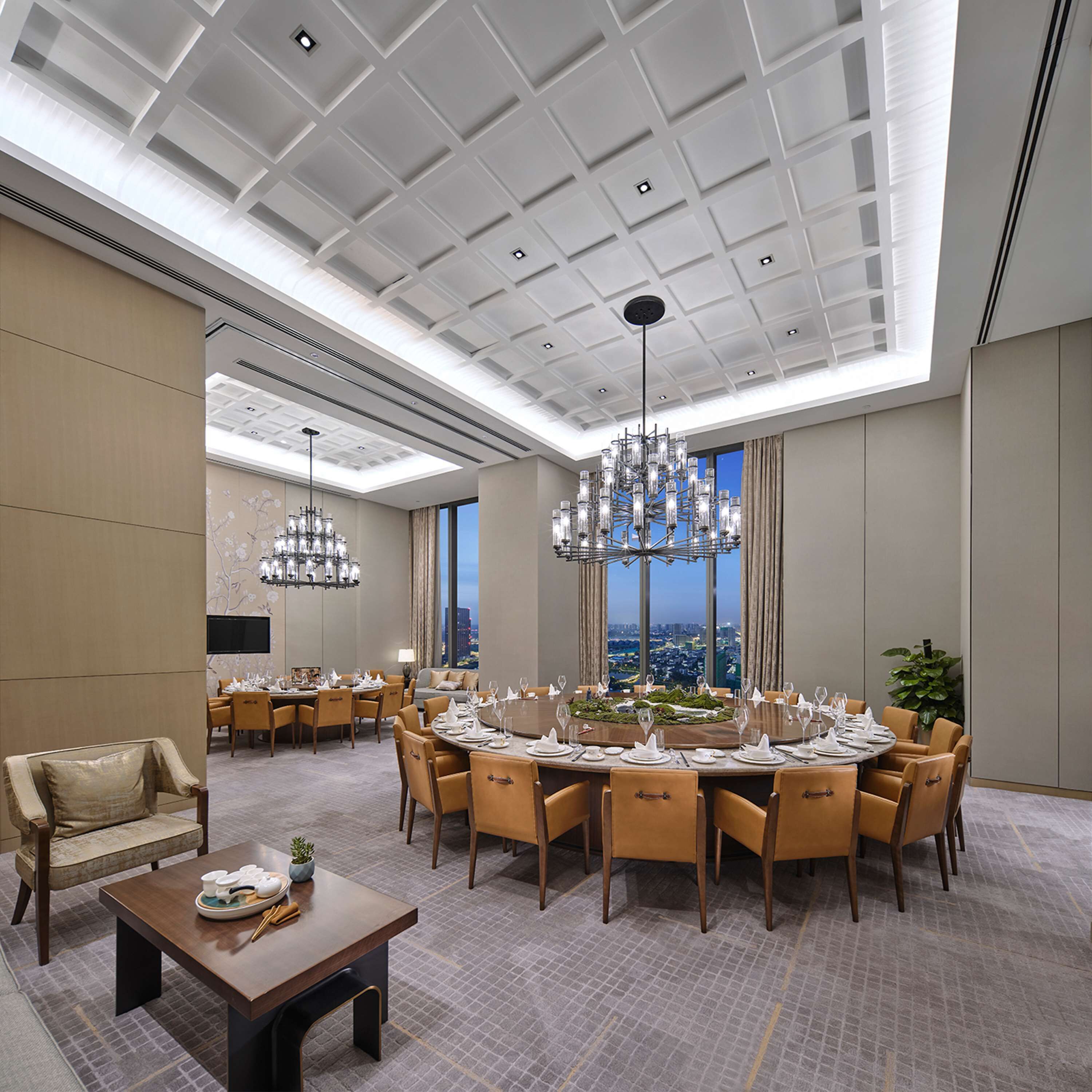 A spacious conference room with a high ceiling, modern chandeliers, and a large round table set for a meeting.