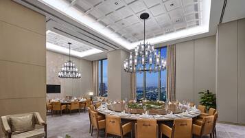 A spacious conference room with a high ceiling, modern chandeliers, and a large round table set for a meeting.