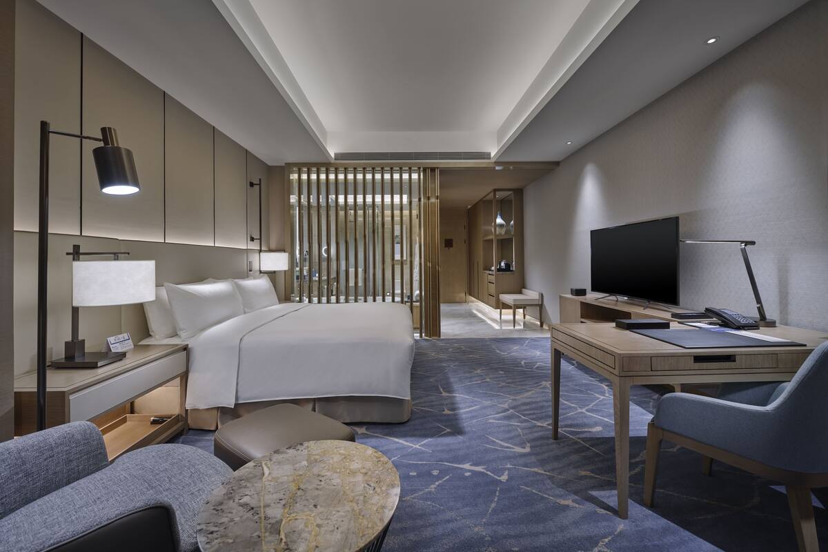 Habitación de hotel con cama, escritorio, televisión y zona de estar.
