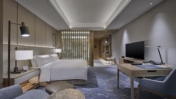 Quarto de hotel moderno com cama, escrivaninha, televisão e área de estar.