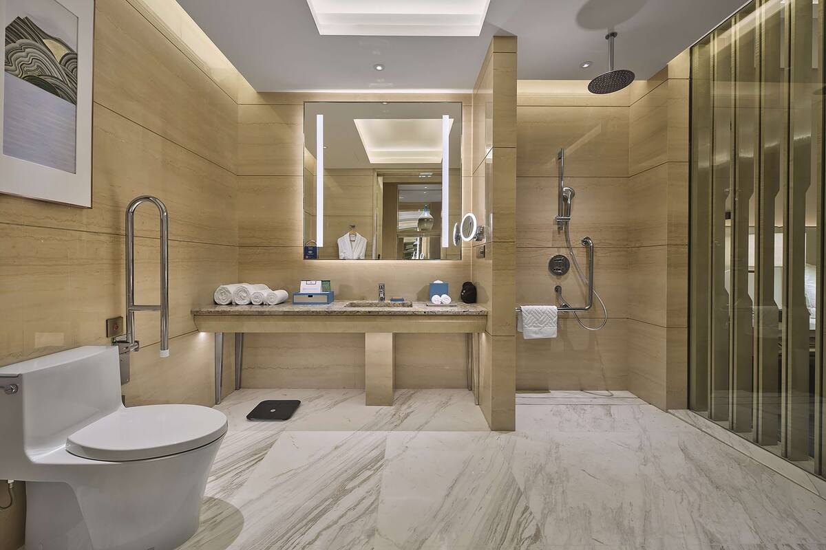 Un baño moderno con inodoro, lavamanos y zona de ducha, que destaca por su suelo de mármol y paredes de madera.