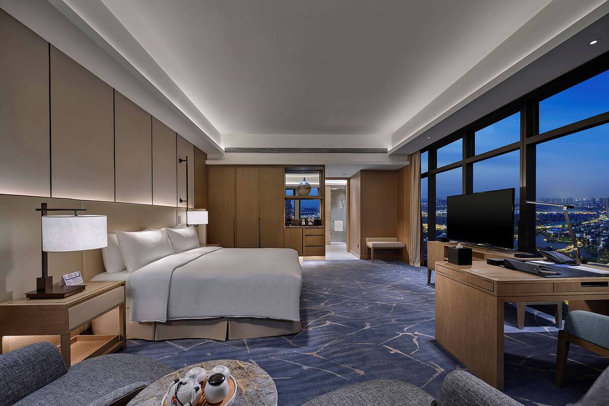 Habitación de hotel moderna con una cama grande, un escritorio con televisión y vista a la ciudad de noche.