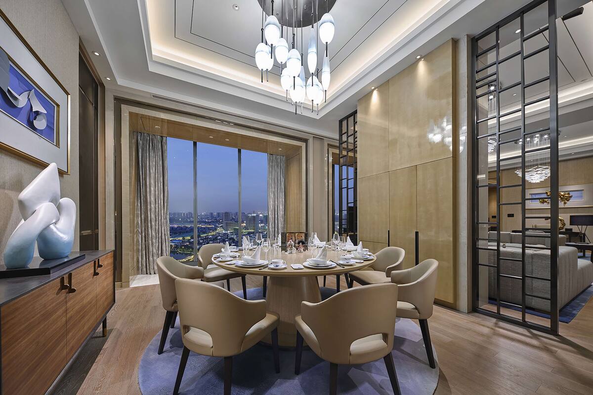 Un comedor moderno con una mesa redonda para seis personas, ventanas amplias que dan a una vista de la ciudad y una araña.